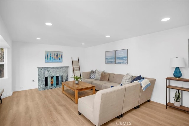 living area with baseboards, light wood-type flooring, a fireplace, and recessed lighting