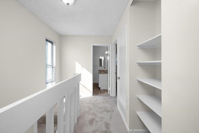 hallway with light colored carpet and a textured ceiling