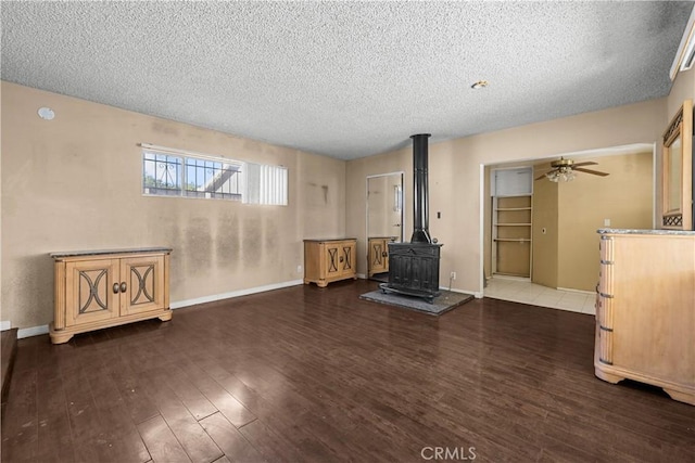 living room featuring ceiling fan, a wood stove, dark wood-type flooring, and a textured ceiling