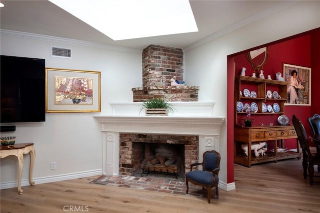 living area featuring hardwood / wood-style flooring, a fireplace, a skylight, and crown molding