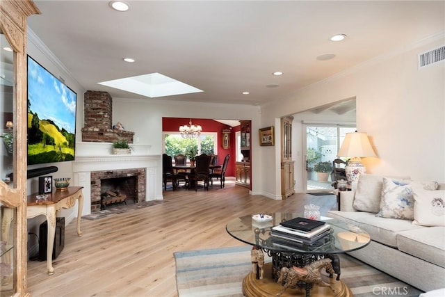 living room featuring a fireplace, a skylight, a notable chandelier, crown molding, and light hardwood / wood-style flooring