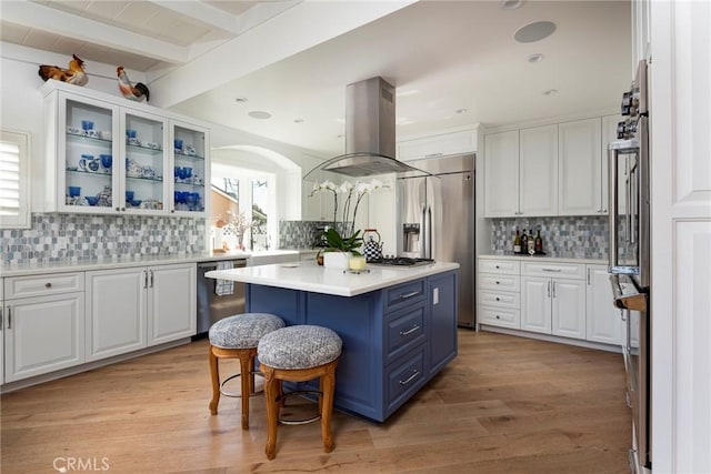 kitchen with appliances with stainless steel finishes, white cabinetry, island exhaust hood, a center island, and blue cabinets