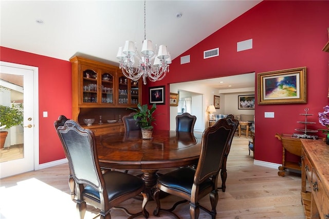 dining area with lofted ceiling, a chandelier, and light hardwood / wood-style flooring