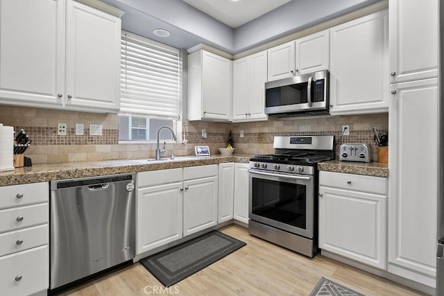 kitchen with sink, white cabinetry, tasteful backsplash, light wood-type flooring, and appliances with stainless steel finishes