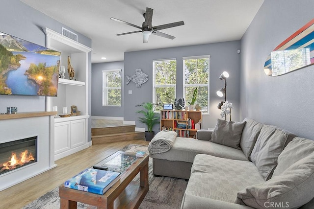 living room featuring ceiling fan, a large fireplace, and light hardwood / wood-style floors