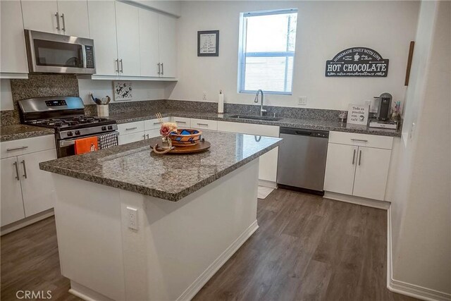 kitchen with sink, appliances with stainless steel finishes, white cabinets, a kitchen island, and dark hardwood / wood-style flooring