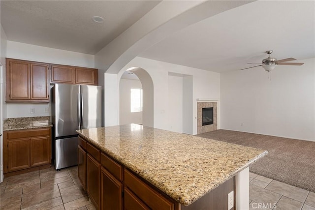 kitchen with light stone counters, a tile fireplace, stainless steel refrigerator, and a kitchen island