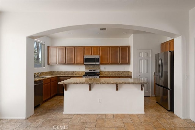 kitchen with light stone counters, stainless steel appliances, a center island, and a kitchen bar