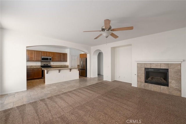 unfurnished living room featuring ceiling fan, light colored carpet, and a tile fireplace