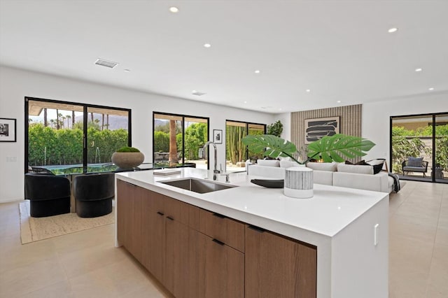 kitchen featuring light tile patterned flooring, sink, a wealth of natural light, and a kitchen island with sink