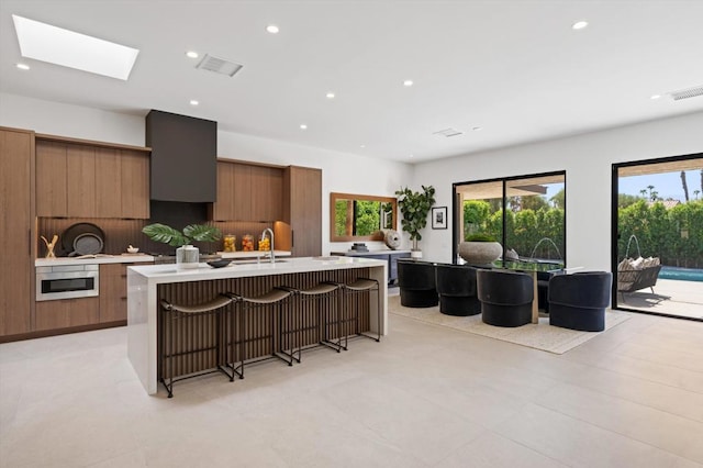 kitchen featuring a breakfast bar, a center island with sink, and a skylight