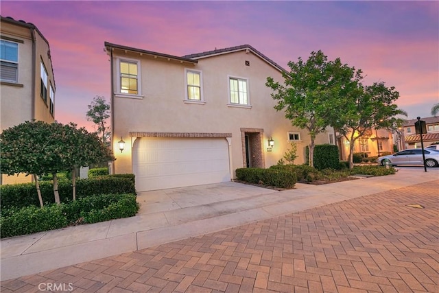 view of front facade featuring an attached garage, decorative driveway, and stucco siding