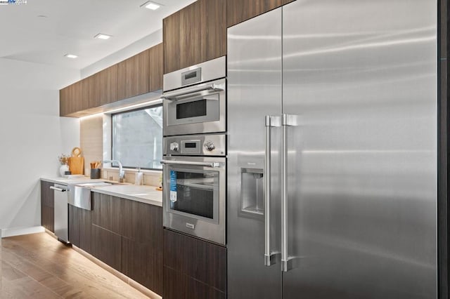 kitchen with appliances with stainless steel finishes, sink, and light wood-type flooring