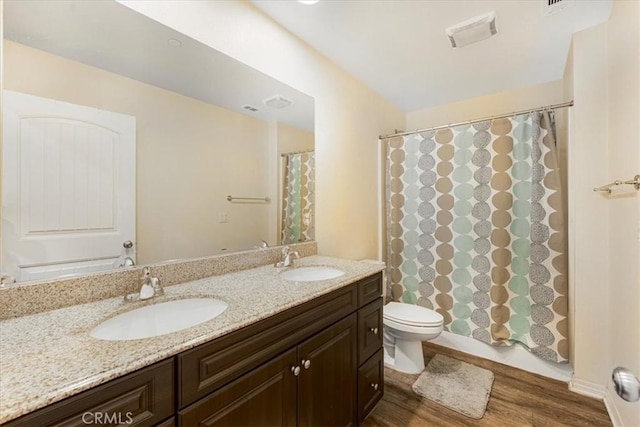 full bath featuring double vanity, wood finished floors, toilet, and a sink