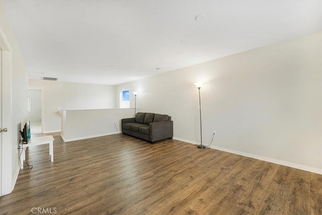 unfurnished room with an upstairs landing, visible vents, baseboards, and wood finished floors