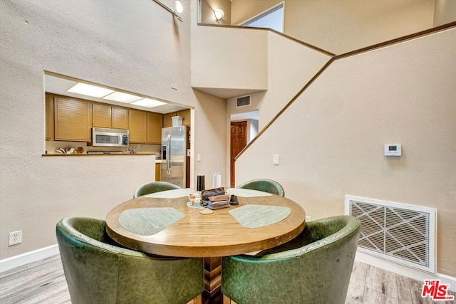 dining area featuring a towering ceiling and light hardwood / wood-style floors