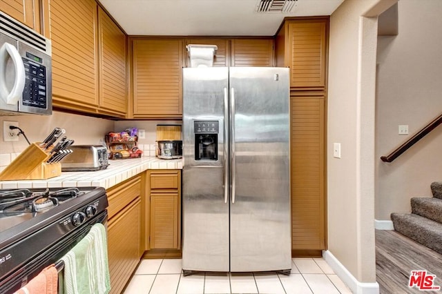 kitchen with light tile patterned floors, tile countertops, and stainless steel appliances