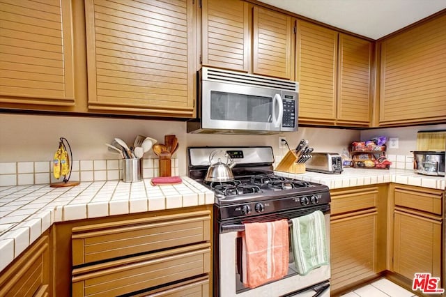 kitchen with light tile patterned floors, tile counters, and stainless steel appliances