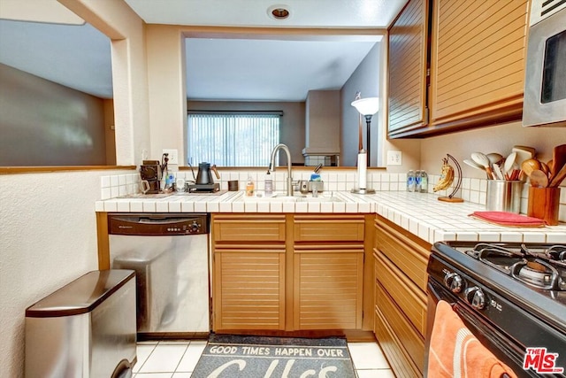 kitchen with sink, light tile patterned floors, tile countertops, and appliances with stainless steel finishes