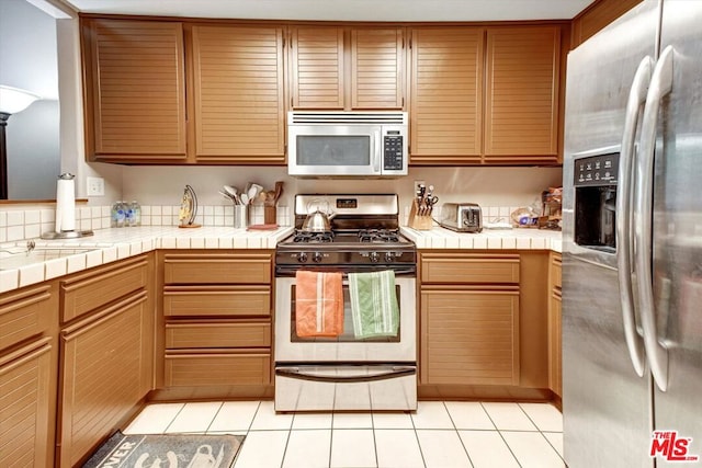 kitchen with appliances with stainless steel finishes, tile counters, and light tile patterned floors