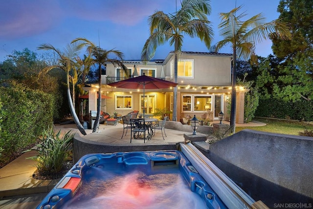 pool at dusk with a hot tub and a patio