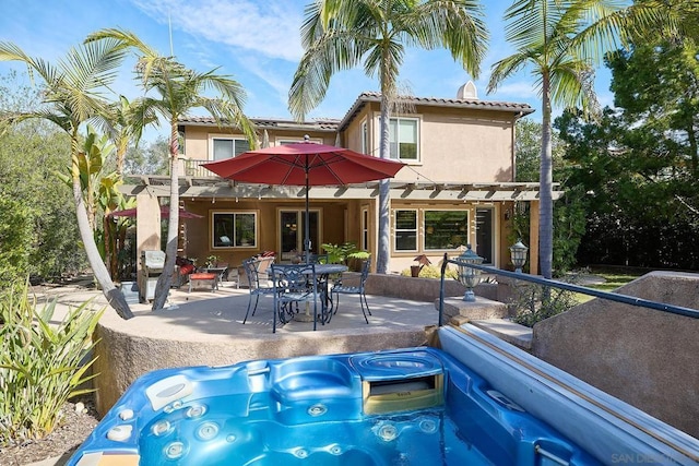 rear view of house with a balcony, a hot tub, a pergola, and a patio