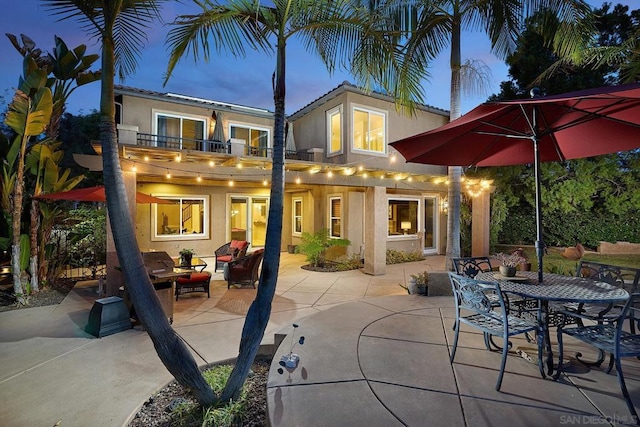 back house at dusk with a balcony, an outdoor hangout area, and a patio area