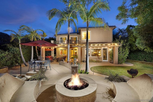 back house at dusk featuring a fire pit, a patio area, and a balcony