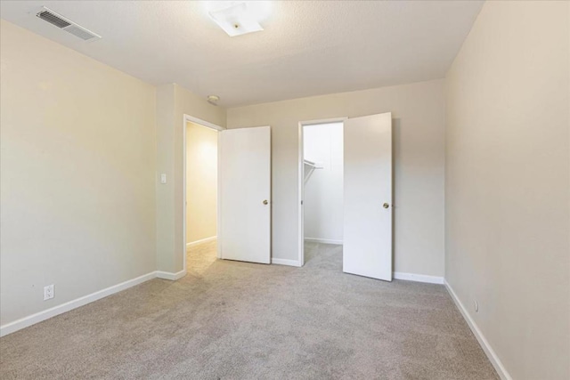 unfurnished bedroom with a walk in closet, light colored carpet, and a closet