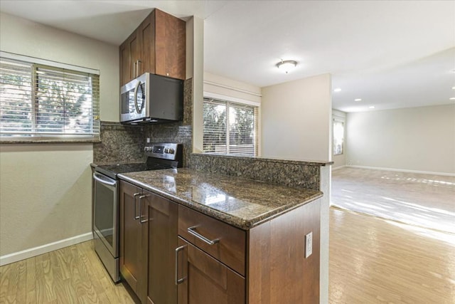 kitchen with light wood-type flooring, appliances with stainless steel finishes, kitchen peninsula, dark stone counters, and decorative backsplash