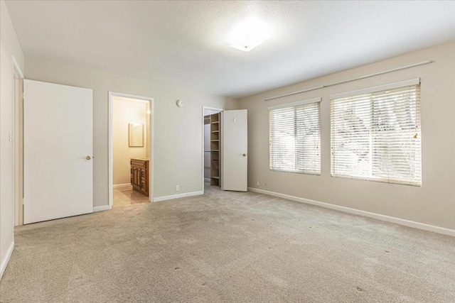 unfurnished bedroom with connected bathroom, a spacious closet, light colored carpet, and a closet