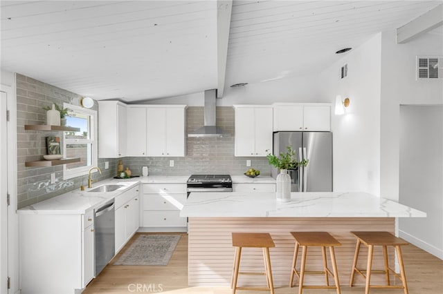 kitchen with sink, wall chimney range hood, a kitchen island, stainless steel appliances, and white cabinets