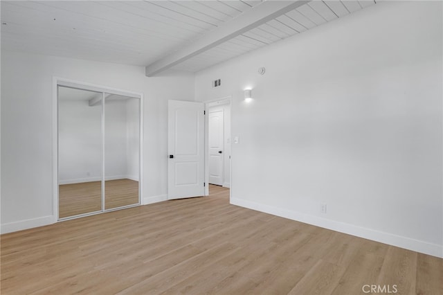 unfurnished bedroom featuring light hardwood / wood-style flooring, lofted ceiling with beams, and a closet