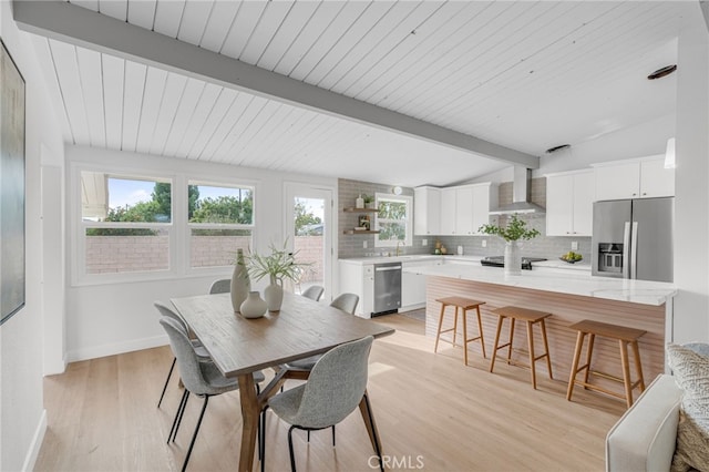 dining space featuring sink, lofted ceiling with beams, and light hardwood / wood-style floors