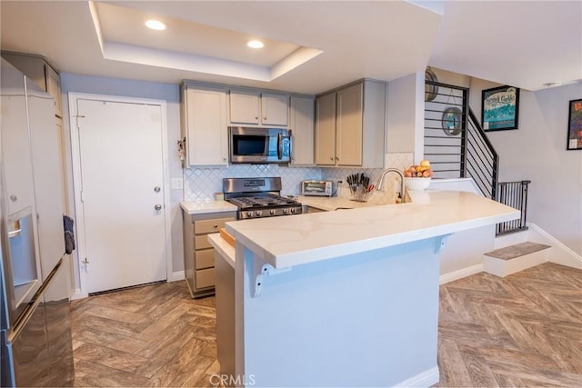 kitchen featuring sink, a breakfast bar area, appliances with stainless steel finishes, a tray ceiling, and kitchen peninsula