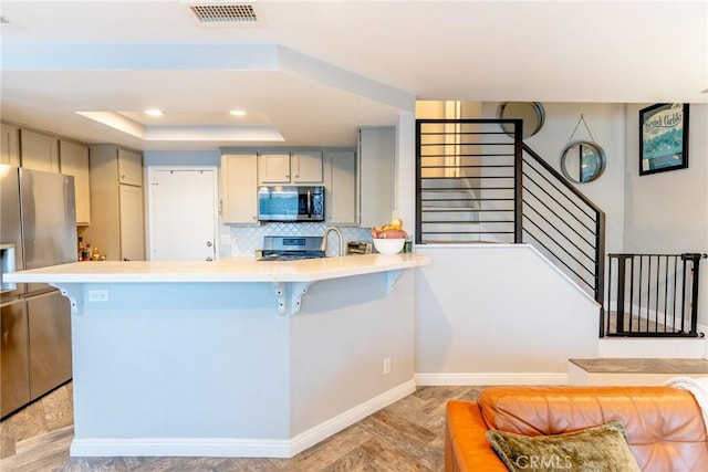 kitchen featuring gray cabinets, appliances with stainless steel finishes, a kitchen breakfast bar, decorative backsplash, and a tray ceiling