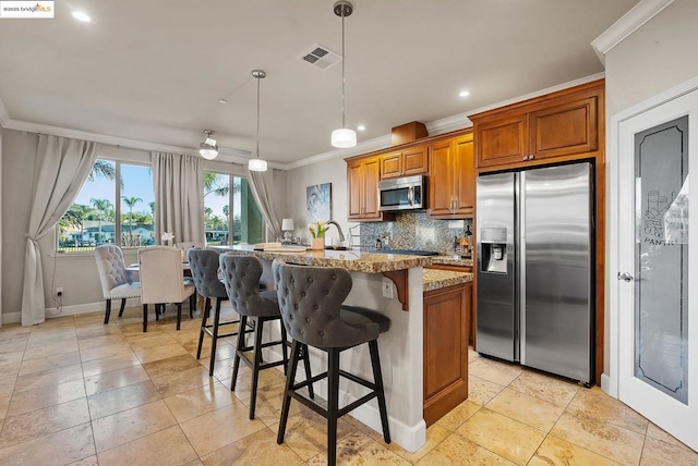 kitchen featuring appliances with stainless steel finishes, hanging light fixtures, ornamental molding, a center island with sink, and decorative backsplash