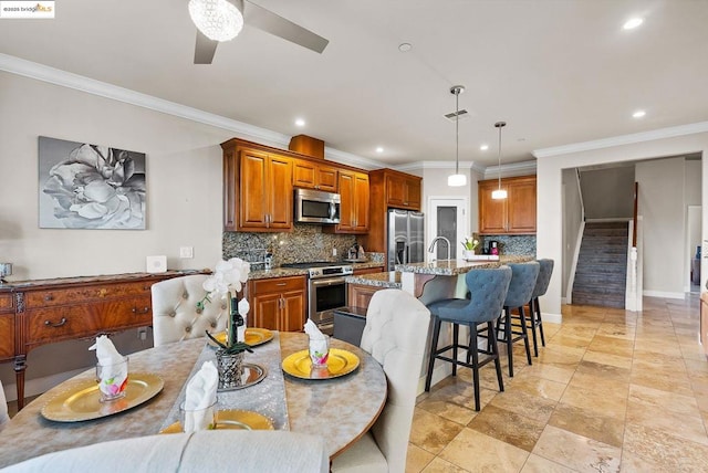 kitchen with tasteful backsplash, hanging light fixtures, stainless steel appliances, light stone countertops, and a center island with sink