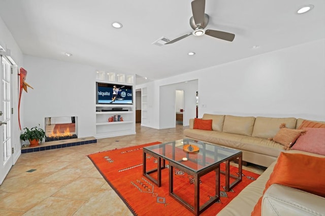 tiled living room featuring a tiled fireplace, built in features, and ceiling fan