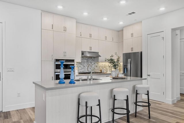 kitchen featuring a kitchen island with sink, stainless steel appliances, light hardwood / wood-style floors, and a breakfast bar