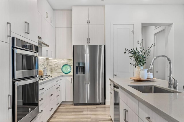 kitchen featuring white cabinetry, sink, decorative backsplash, stainless steel appliances, and light hardwood / wood-style flooring