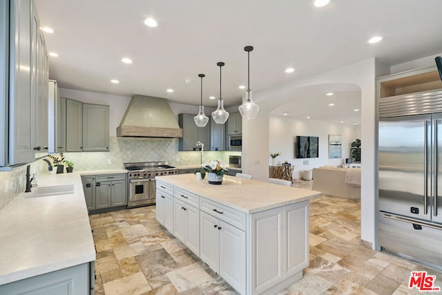 kitchen with premium range hood, sink, built in appliances, a center island, and gray cabinets