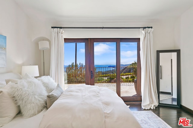 bedroom with multiple windows, access to exterior, dark hardwood / wood-style floors, and a water view