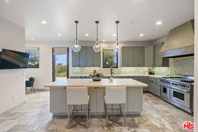 kitchen with sink, a kitchen island, custom range hood, pendant lighting, and range with two ovens