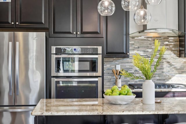 kitchen with light stone countertops, appliances with stainless steel finishes, wall chimney range hood, and decorative backsplash