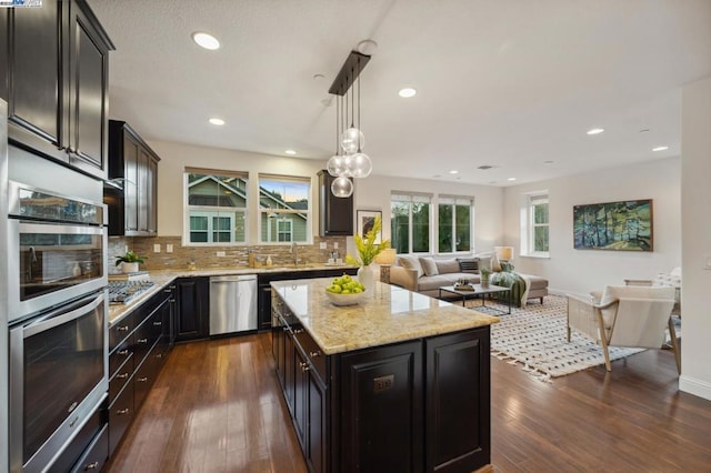 kitchen with hanging light fixtures, stainless steel appliances, dark hardwood / wood-style floors, a center island, and decorative backsplash