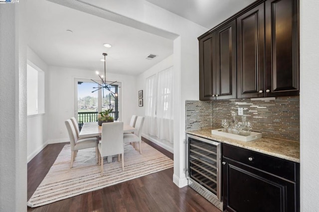 dining area featuring dark hardwood / wood-style flooring, beverage cooler, a chandelier, and indoor bar