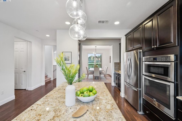 kitchen with hanging light fixtures, light stone countertops, appliances with stainless steel finishes, and dark wood-type flooring