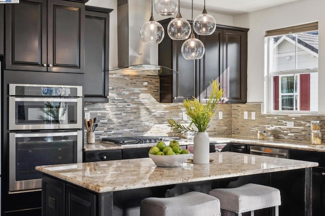 kitchen featuring a breakfast bar, hanging light fixtures, a kitchen island, stainless steel appliances, and wall chimney range hood