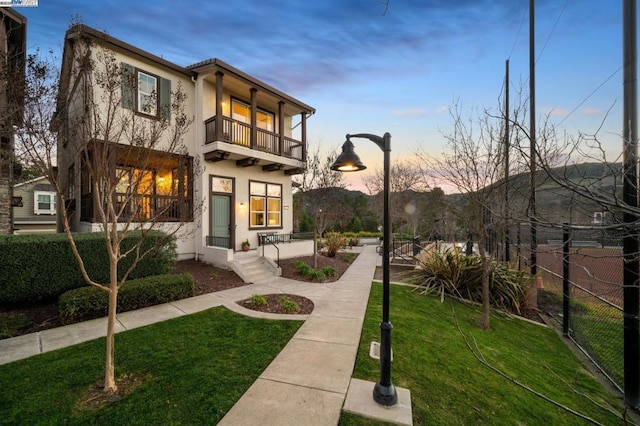 back house at dusk featuring a lawn and a balcony